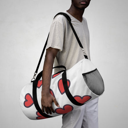 Person holding a white duffel bag with red heart patterns against a plain background