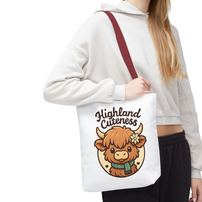 Person holding a tote bag with a cartoon Highland cow and 'Highland Cuteness' text.