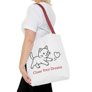 Person holding a white tote bag with a cat illustration and text on a white background