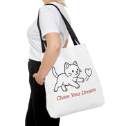 Person holding a white tote bag with a cat illustration and 'Chase Your Dreams' text.