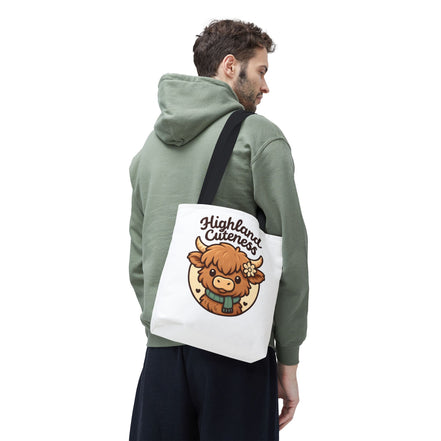 Person wearing a green hoodie with a white tote bag featuring a Highland cow design on a white background