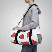 Person carrying a white duffel bag with red hearts on a plain background