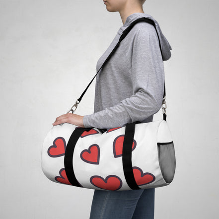 Person carrying a white duffel bag with red hearts on a plain background