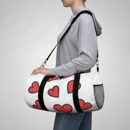 Person carrying a white duffel bag with red hearts on a plain background