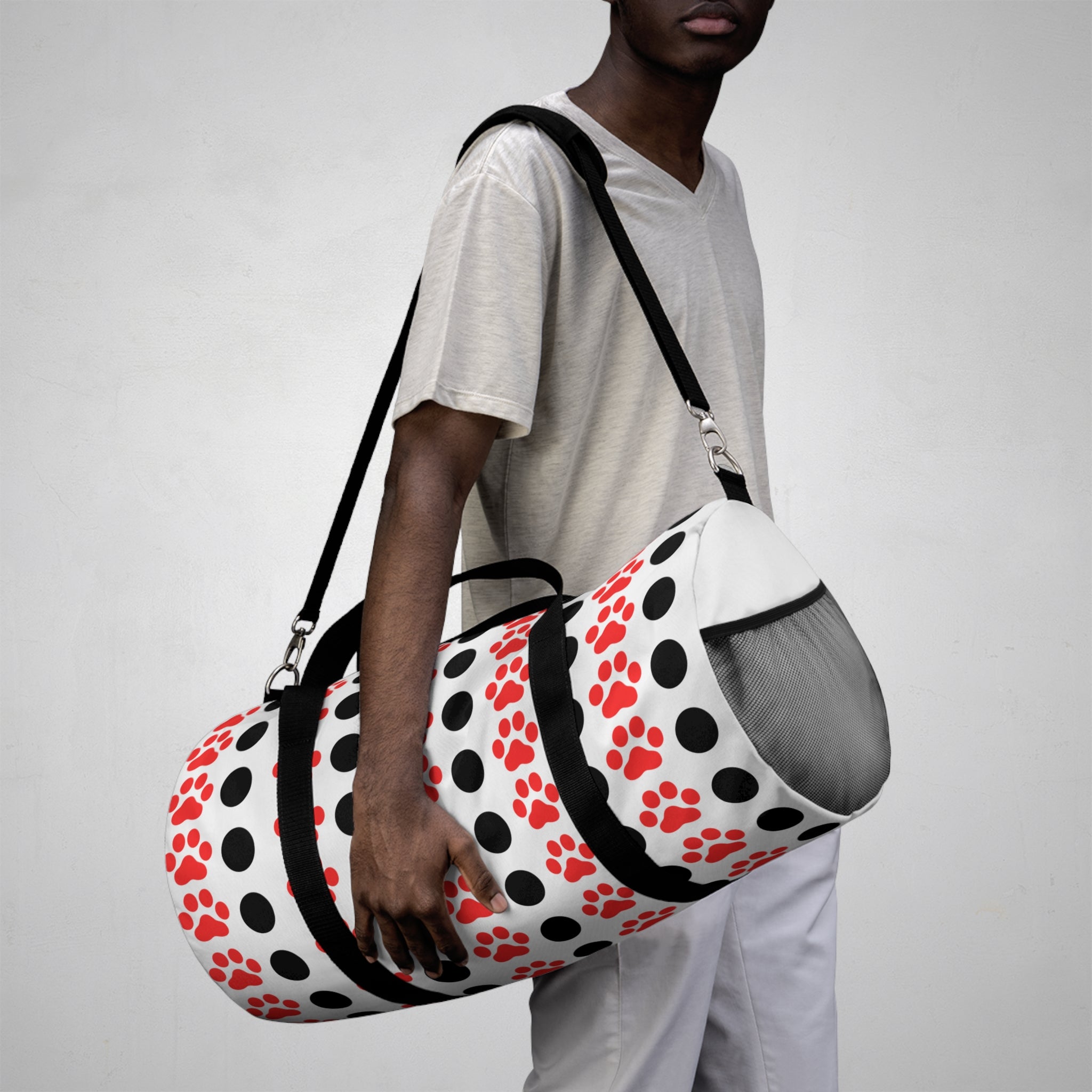 Person holding a duffel bag with red paw prints on a plain background