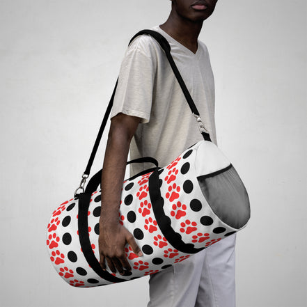 Person holding a duffel bag with red paw prints on a plain background