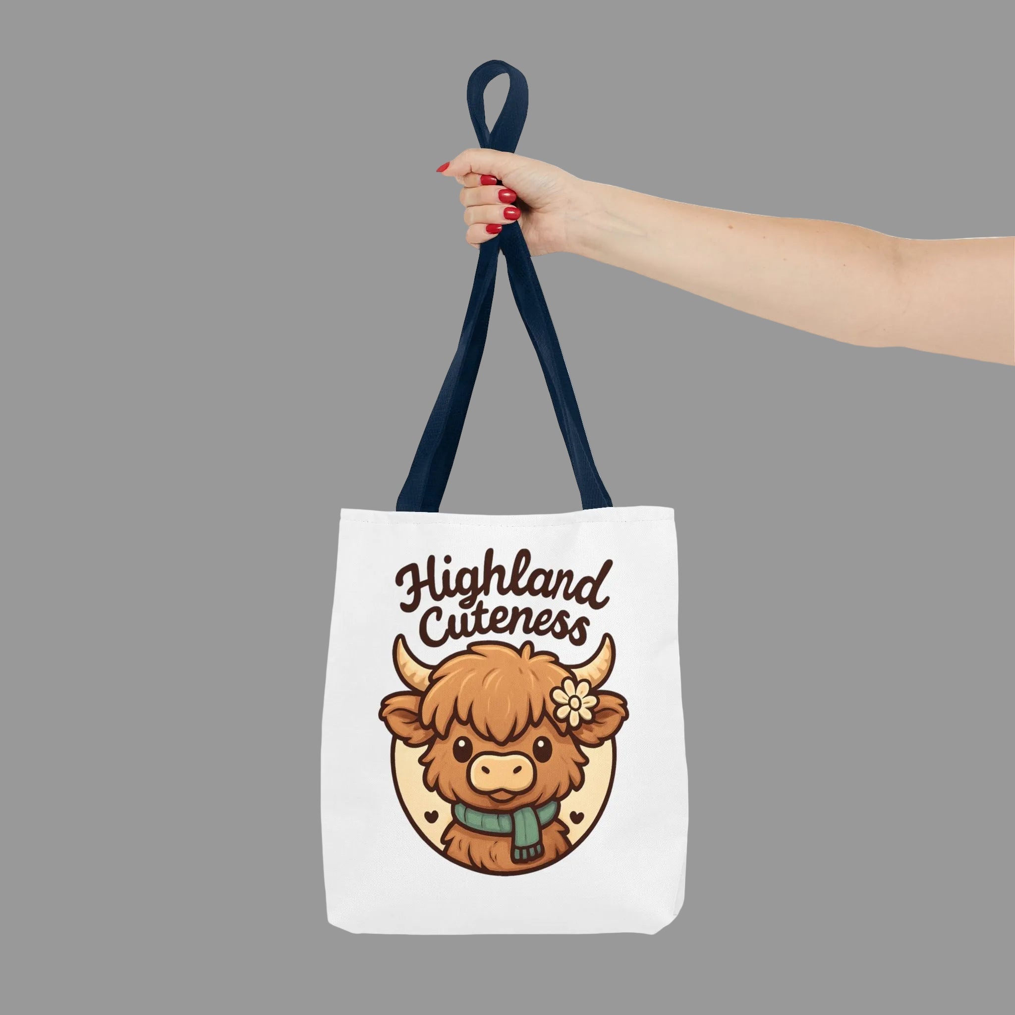 Highland Cuteness tote bag with adorable Highland cow graphic design. Tote bag with a cartoon highland cow and 'Highland Cuteness' text, held by a hand.