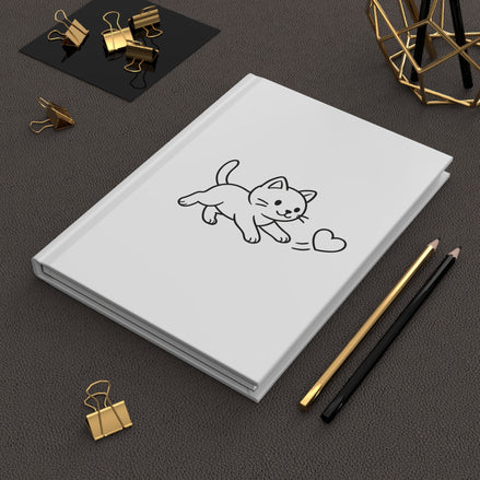 White notebook with a black line drawing of a cat on a dark surface with stationery items.