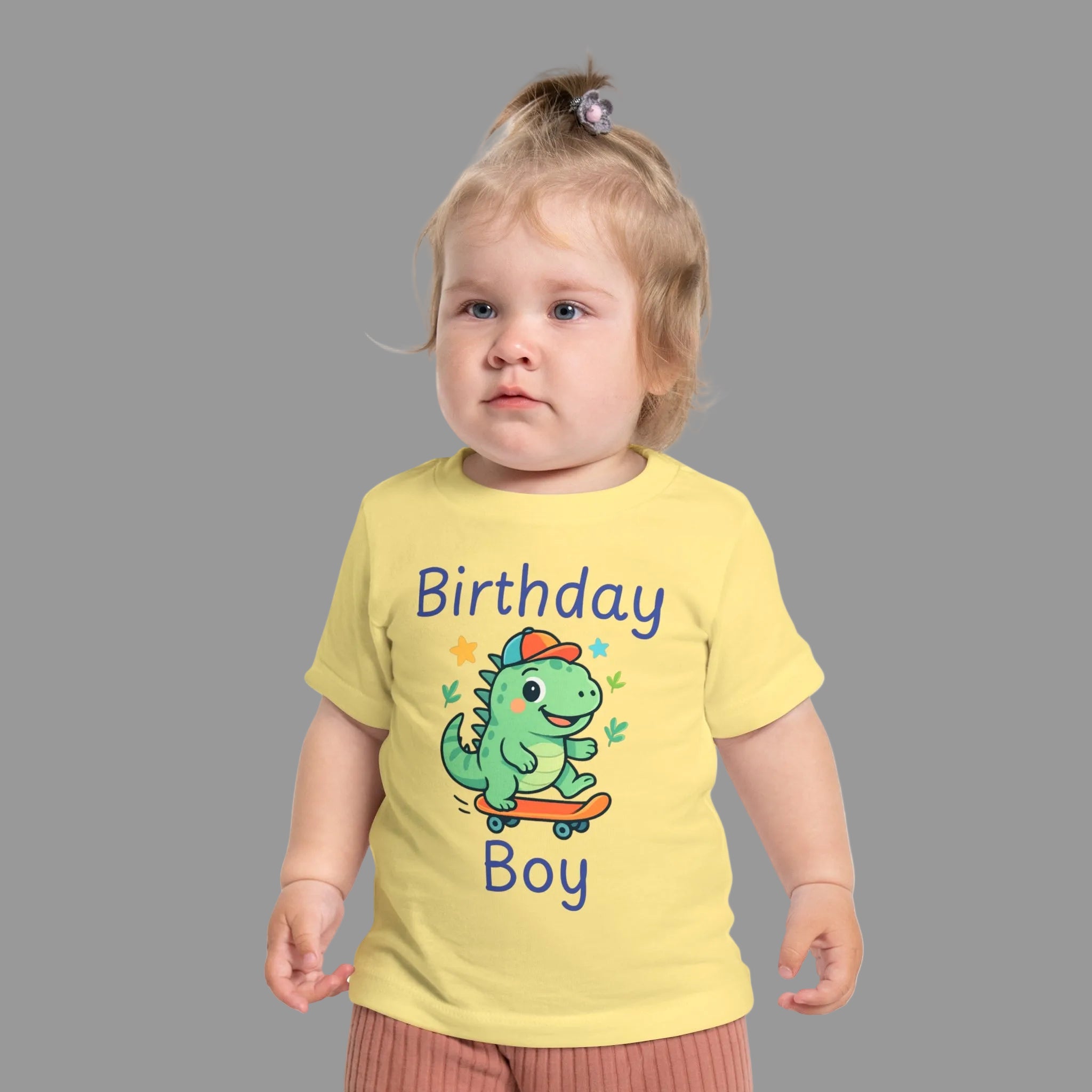 Birthday Boy baby t-shirt with cute skateboarding dinosaur first birthday design. Child wearing a yellow t-shirt with a dinosaur graphic and text on a white background