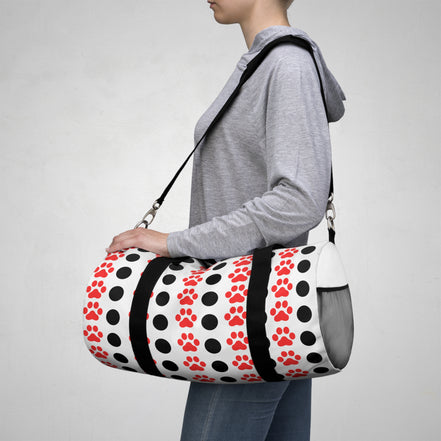 Person carrying a duffel bag with polka dot and paw print design on a plain background