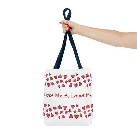 Tote bag with red heart pattern and text 'Love Me or Leave Me' held by a hand on a white background