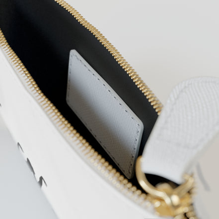 Close-up of a white handbag with gold zipper and handle.